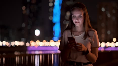 Young-woman-tourist-travels-through-the-night-megalopolis-and-writes-text-messages-on-social-networks-about-the-journey-holds-the-phone-in-her-hands-and-looks-at-the-screen-of-the-gadget